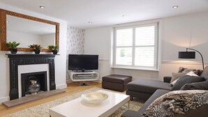 A modern living room with a fireplace, a flat-screen TV, a sofa, and a large window.