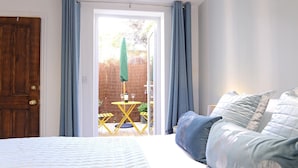A bedroom with a bed, a window with curtains, and a view of an outdoor area with a table and chairs.