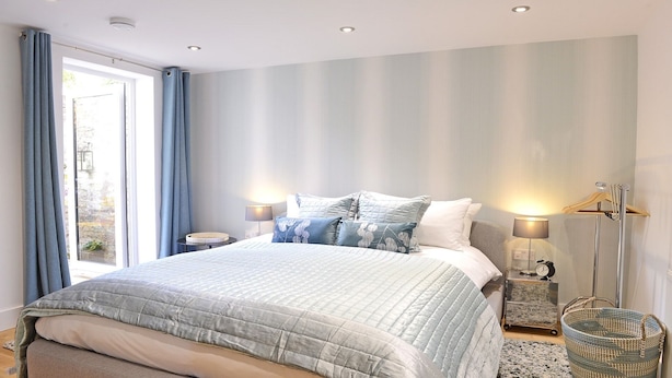 A bedroom with a large bed, two bedside tables, a floor lamp, and a window with curtains.