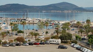 A marina with boats, parked cars, and palm trees. - attic with stunning views (Alghero)