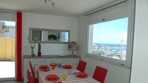 A dining area with a table set for four, red chairs, a red and white checkered tablecloth, and a view of the city through a large window. - attic with stunning views (Alghero)