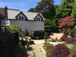 A two-story house with a gravel driveway and a garden with various plants and flowers.