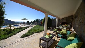 A covered outdoor seating area with a pool view, green cushions, and a stone-tiled patio. - Awesome Coastal Views, Infinity Pool & BBQ area, Very Private Family Villa  (Monchique)