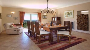 A dining area with a table set for four, surrounded by wooden chairs, a chandelier, and a view of the outdoors.