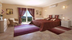 A bedroom with a large bed, a chair, a nightstand, and a view of the outdoors.