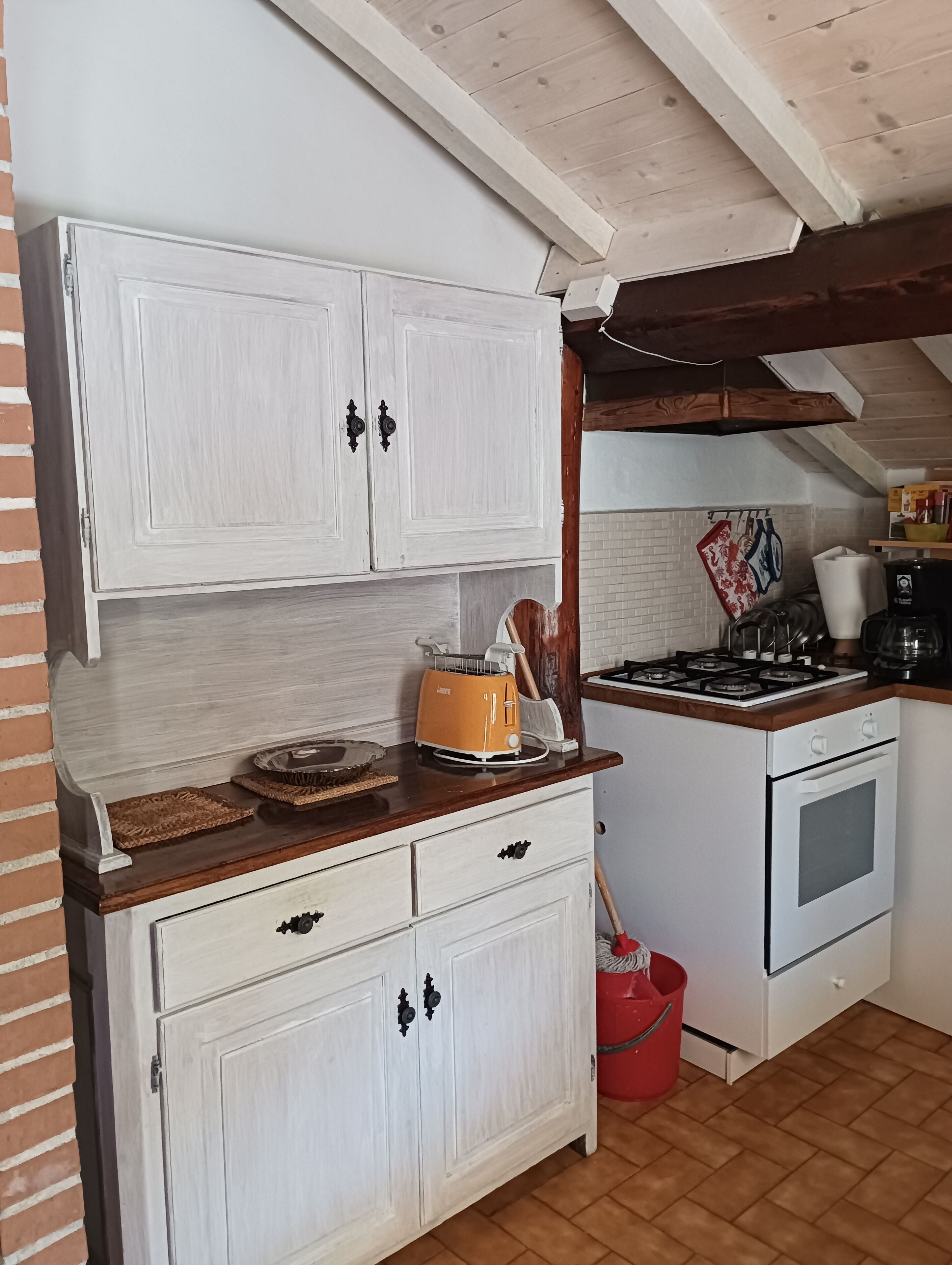 A kitchen with white cabinets, a wooden countertop, a stove, and a red bucket.