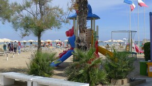 Een strand met een speeltuin, palmbomen en strandparasols.