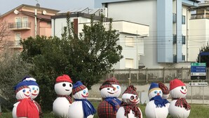 Een rij sneeuwmensen met sjaals en mutsen, geplaatst op gras voor een woongebouw.