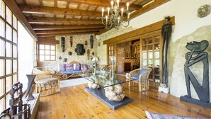 Una habitación amplia con pisos de madera, un candelabro, muebles de mimbre y paredes de piedra.