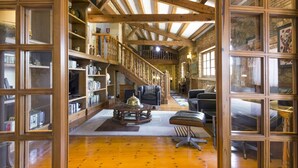 Una habitación espaciosa con vigas de madera, una escalera y un rincón de descanso acogedor con chimenea.