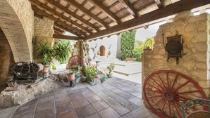 Un patio rústico con muros de piedra, techo de madera y una gran rueda roja.