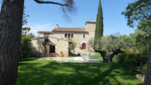 Una casa de piedra con techo de tejas, piscina y un jardín bien cuidado.