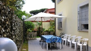 Um pátio com mesa e cadeiras, um guarda-sol branco e uma parede decorativa.