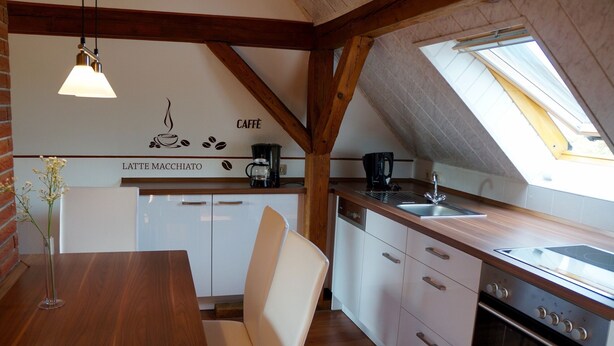 Une cuisine avec des meubles blancs, un plan de travail en bois, une machine à café et une lucarne.