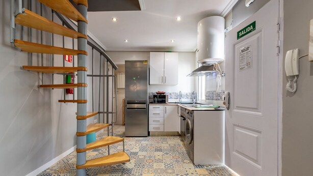 A modern kitchen with a stainless steel refrigerator, a built-in oven, and a washing machine. There is a staircase with wooden steps and a metal railing. A 'SALIDA' sign is visible on the door. - Townhouse near Plaza Castilla - Apartment CUZCO (Madrid)