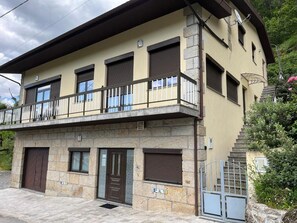 Un edificio de dos pisos con balcón, fachada de piedra y una escalera que lleva a un nivel superior.