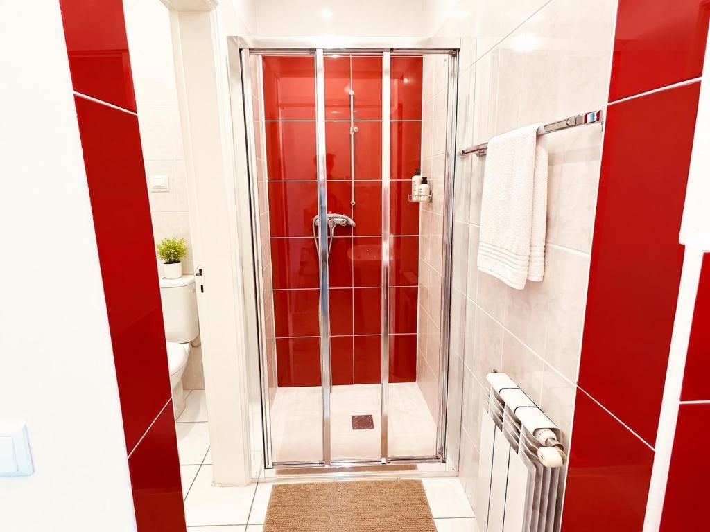 Un baño moderno con ducha envuelta en vidrio, inodoro blanco y pared de azulejos rojos.
