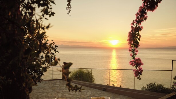 Een terras met uitzicht op de zonsondergang over het water, een plantentafel en een stoel.