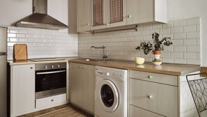 Een moderne keuken met witte kasten, een roestvrijstalen afzuigkap, een inbouwoven, een wasmachine en een houten aanrecht met een bloempot.
