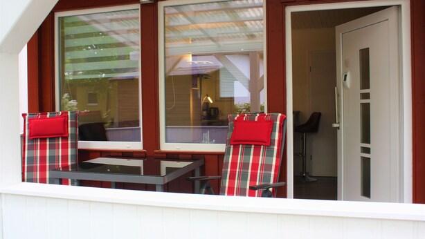 A balcony with two plaid chairs and a table, a door leading inside, and a window with a view of the outside. - Bungalow "Morgenrot", 250 m to the Müritz & jetty, alternative form of payment possible (Röbel/Müritz)