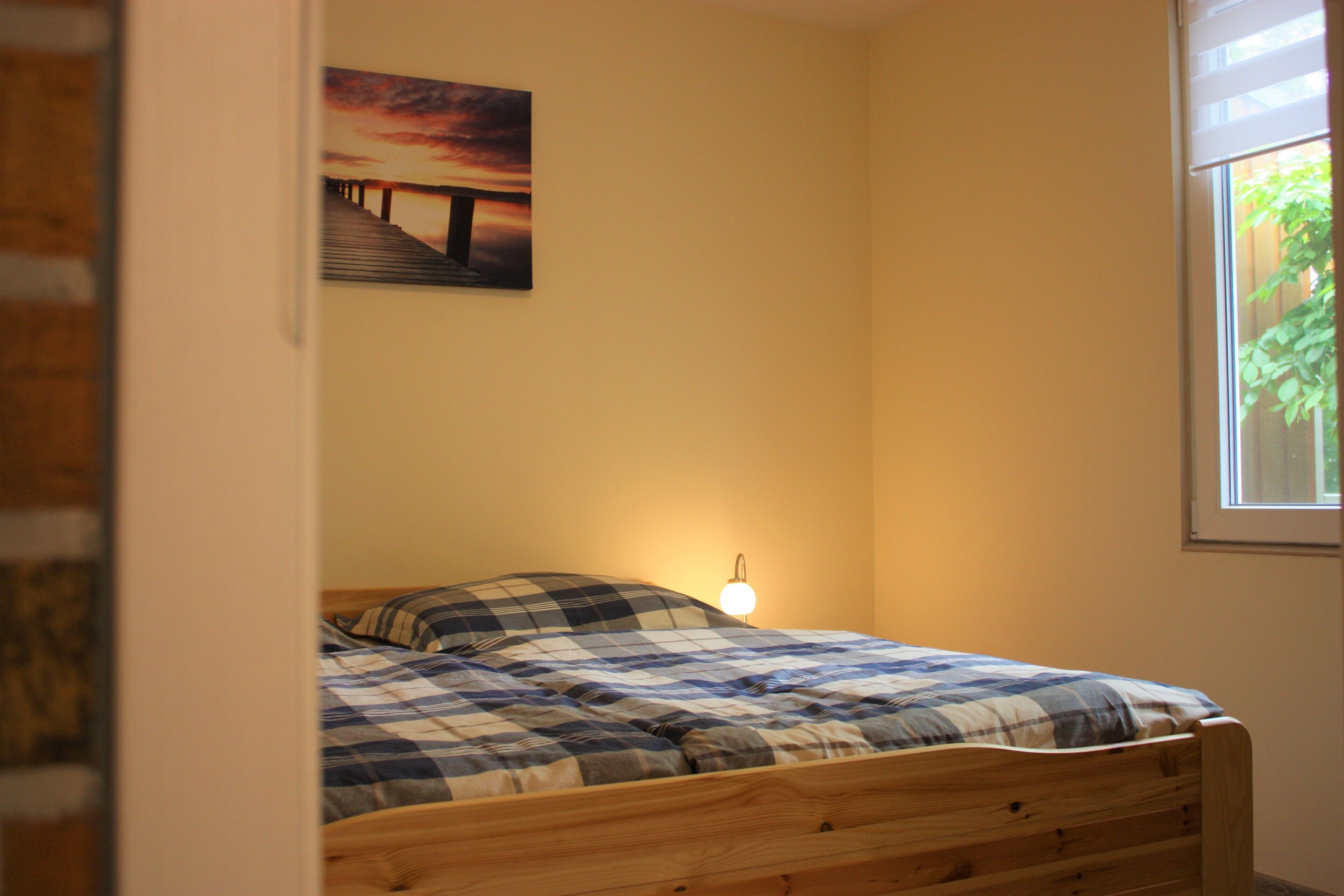A bedroom with a bed, a wall-mounted picture, and a window.