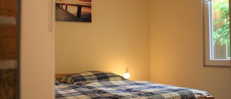 A bedroom with a bed, a wall-mounted picture, and a window.