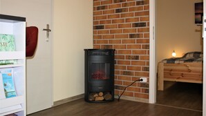 A room with a brick wall, a wooden bed, and a black wood-burning stove. - Bungalow "Morgenrot", 250 m to the Müritz & jetty, alternative form of payment possible (Röbel/Müritz)