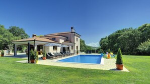 Une maison à deux étages avec une piscine, un espace salon extérieur et des plantes en pot.