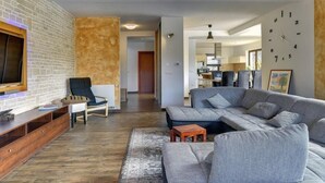 Un salon moderne avec un canapé d’angle, un téléviseur et un meuble de rangement en bois.