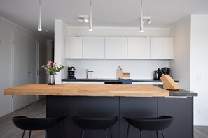 A modern kitchen with a wooden island, black bar stools, white cabinets, and pendant lighting. - Design penthouse apartment on the steinwarder with its own sauna (Heiligenhafen)