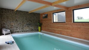 Una piscina amb parets de pedra i bigues de fusta, una cadira i una planta en test.