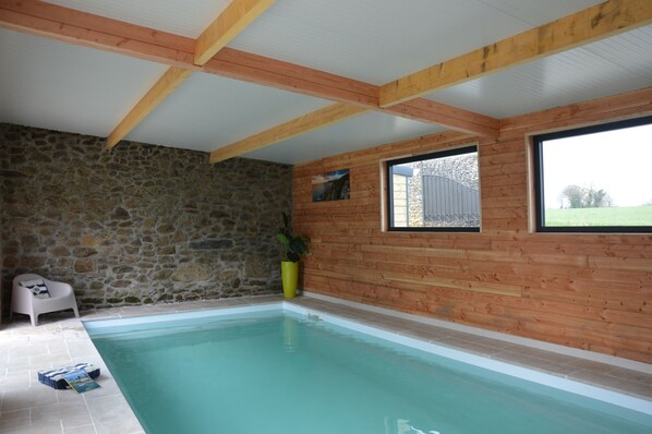 Una piscina con paredes de piedra y vigas de madera, una silla y una planta en maceta.
