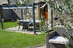 Eine Terrasse im Freien mit Tisch und Stühlen, einem Korbsessel und einem Steinhaus im Hintergrund.