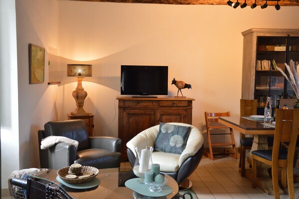 A living room with a television, a lamp, a bookshelf, and a dining area. - Swimming pool NOTHING BUT FOR YOU, covered, heated, 6 pers near St Malo BRETAGNE (plancoet)