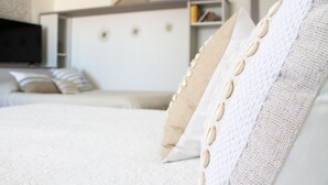 Een netjes opgemaakt bed met een combinatie van witte en beige kussens, een wit hoofdbord, en een televisie op de achtergrond.