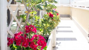 Een balkon met een wit lattenwerk, plantenbakken en rode bloemen.