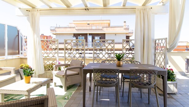 Een overdekt terras buiten met rieten meubels, een tafel en potplanten.