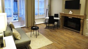 A living room with a sofa, chairs, a fireplace, a TV, and large windows with curtains. - Studio Vieux Lyon  (Lyon)