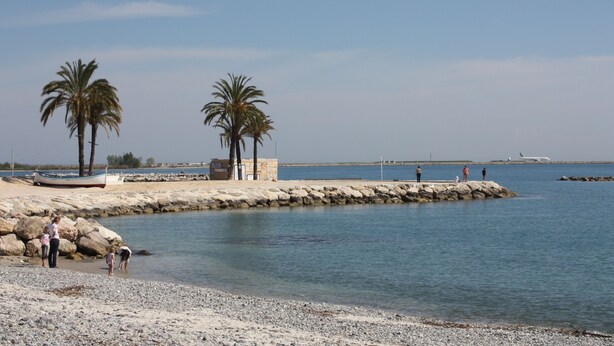 Una spiaggia con palme, un molo roccioso e una barca.