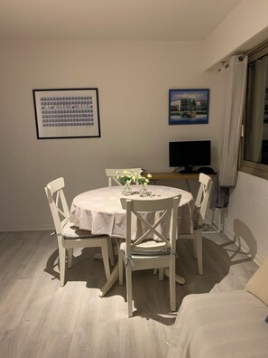 A dining area with a round table, white chairs, and a TV on a stand.