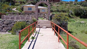 A pathway leading to a building with a stone archway, surrounded by greenery and a clear blue sky. - Casa de Valentin (Capachica)