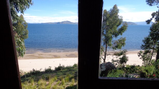 A view of a beach through a window, with a clear sky and distant mountains. - Casa de Valentin (Capachica)