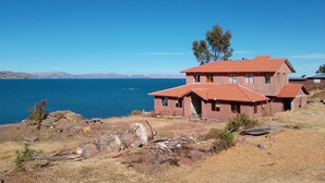 A two-story house with a red-tiled roof, situated by a body of water with mountains in the distance. - Casa de Valentin (Capachica)