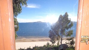 A beach view through a wooden door with a metal latch, a tree, and a clear sky. - Casa de Valentin (Capachica)