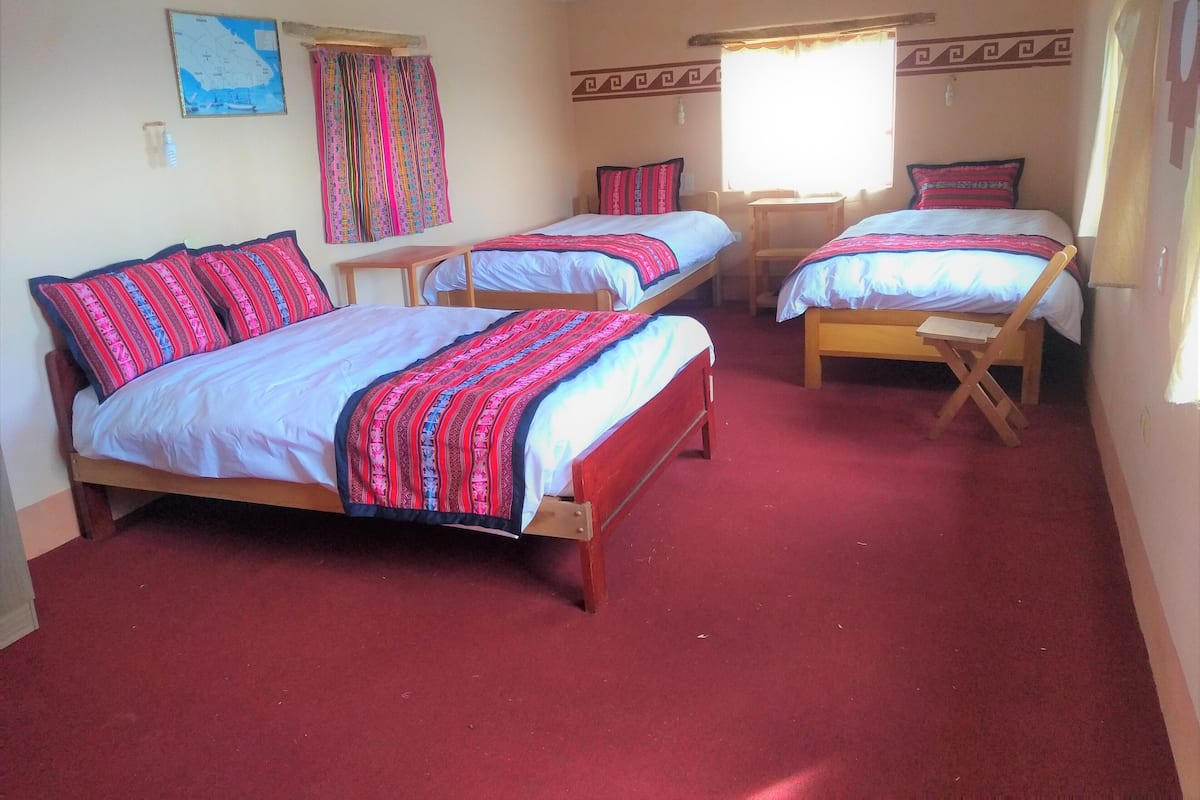 A room with three wooden beds, each with a red and white patterned bedspread. There is a map on the wall and a window with curtains.