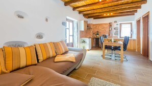 A cozy living room with a wooden ceiling, a sofa with striped cushions, a dining area with a table and chairs, and a kitchen with a tiled backsplash. - Beautiful holiday house KORNIC (Kornić)
