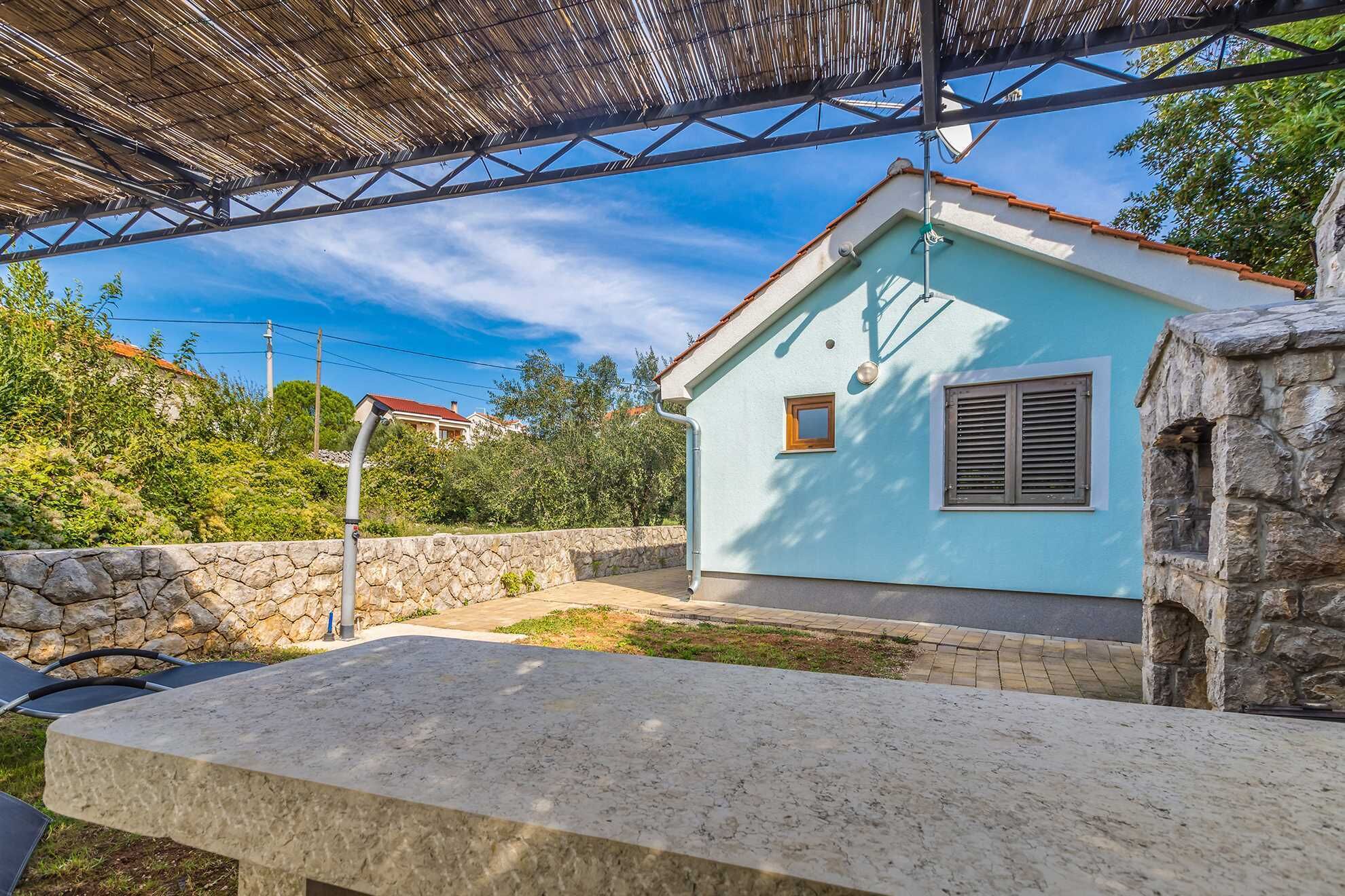 A light blue house with a stone wall, a stone bench, and a metal pergola structure.