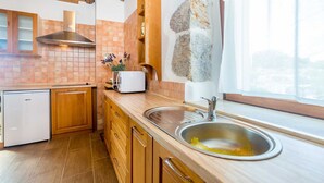 A kitchen with wooden cabinets, a white refrigerator, a built-in oven, and a stone accent wall. - Beautiful holiday house KORNIC (Kornić)