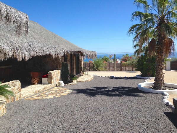 A thatched-roof building with a stone exterior, a gravel driveway, and a palm tree. - Villa Pitaya Best beach in El Sargento Lexury Palapas la Choya Ocean View. (El Sgto)