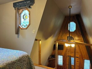 Cozy cabin room with a sloped ceiling, wooden beams, and a window featuring a geometric pattern.